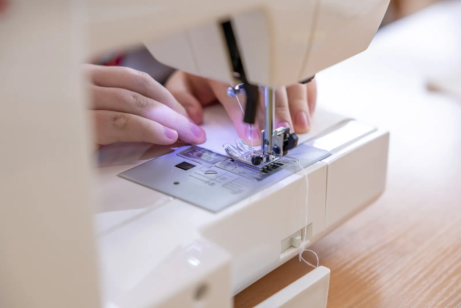 Hands guiding fabric under a sewing machine needle