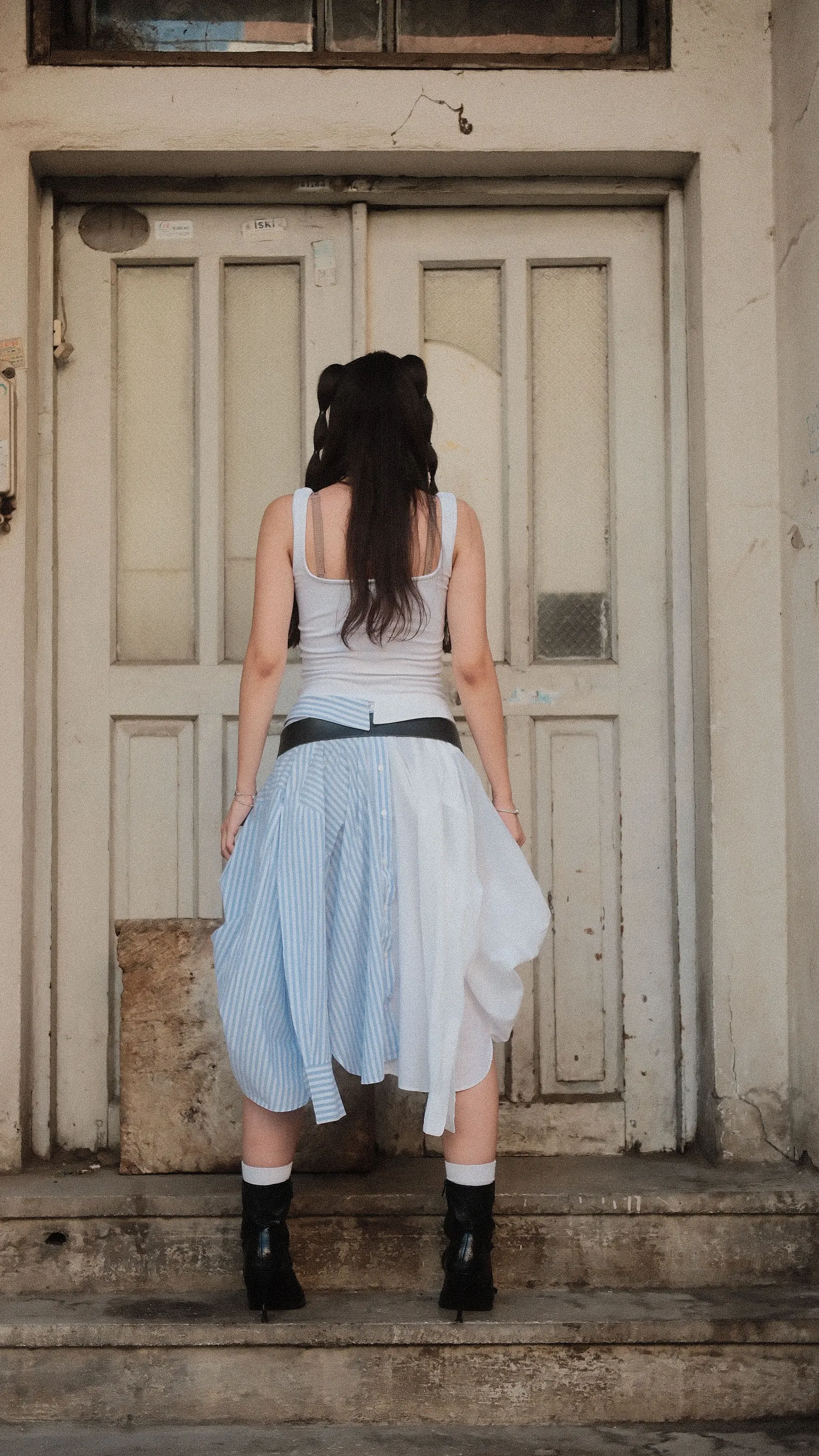 A woman seen from behind in a light skirt, standing at a weathered wooden door