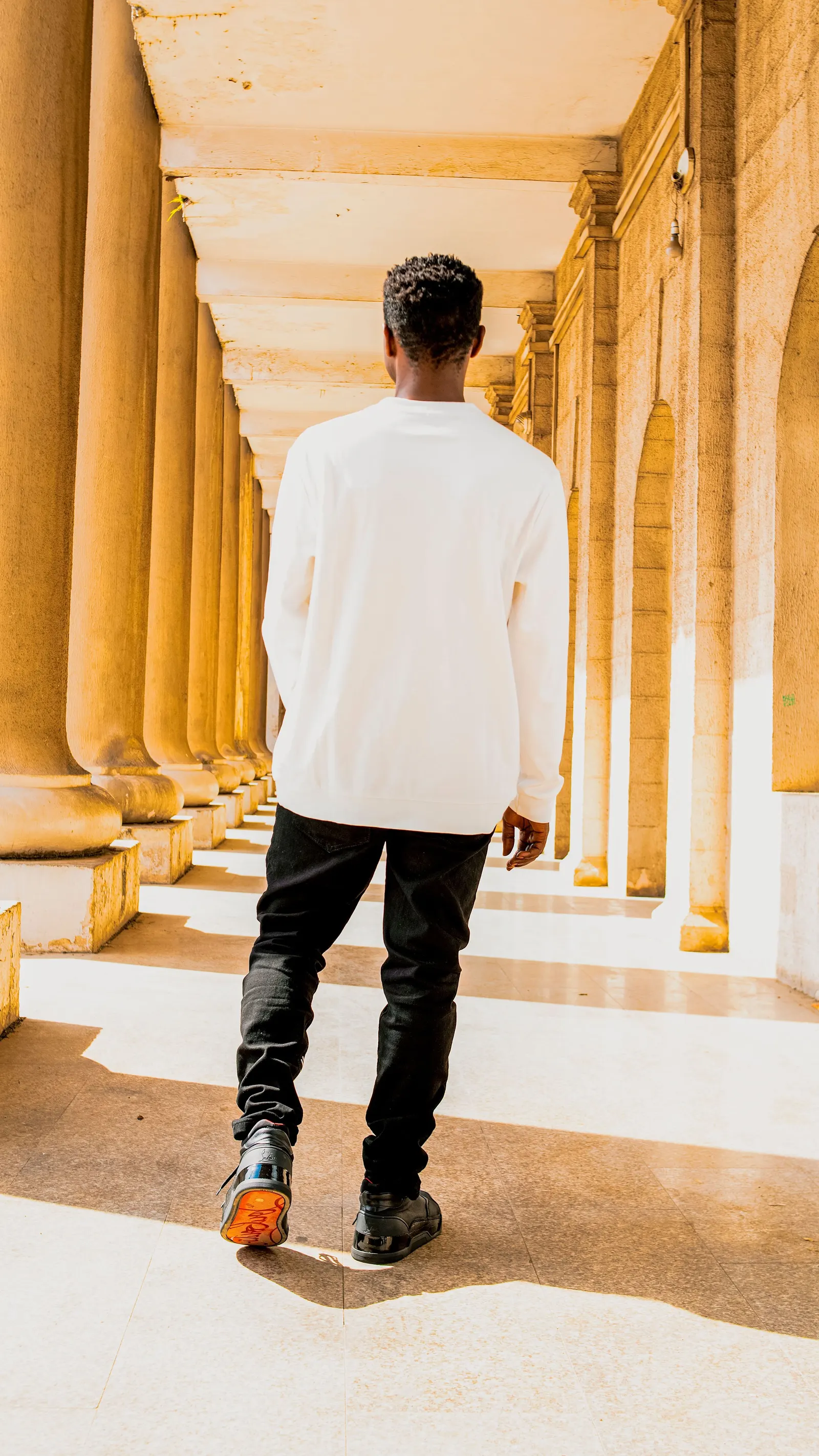 A man in a white shirt walking away through a sunlit stone arcade