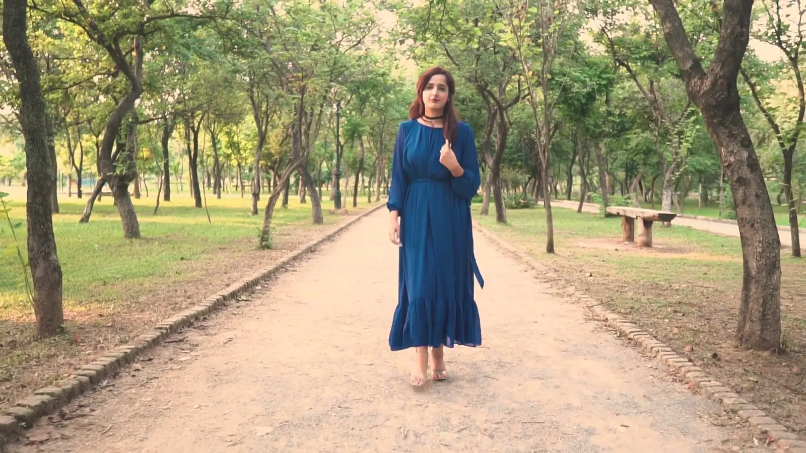 A woman in a long blue dress walking along a tree-lined park path
