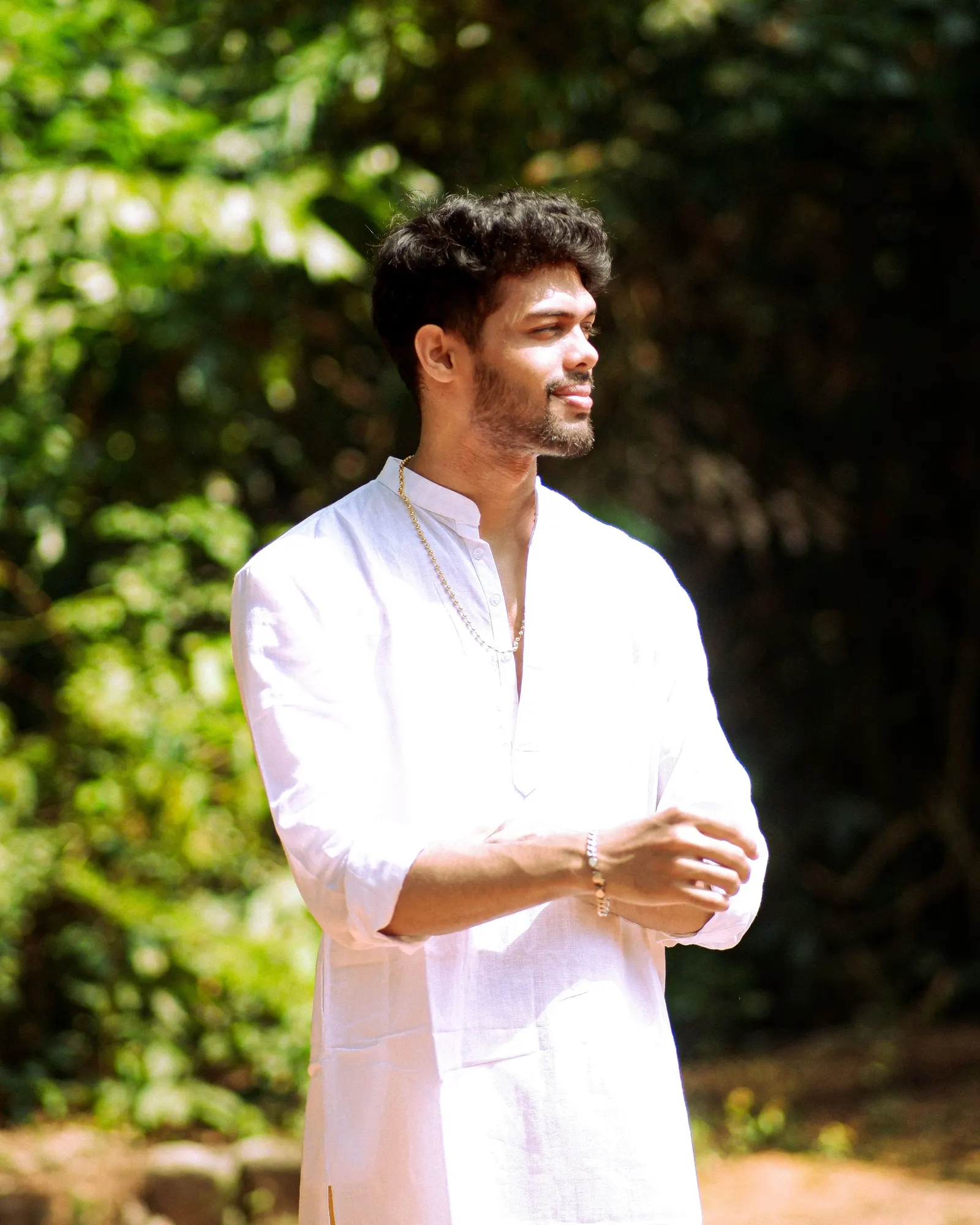 A man in a white kurta standing in dappled green light