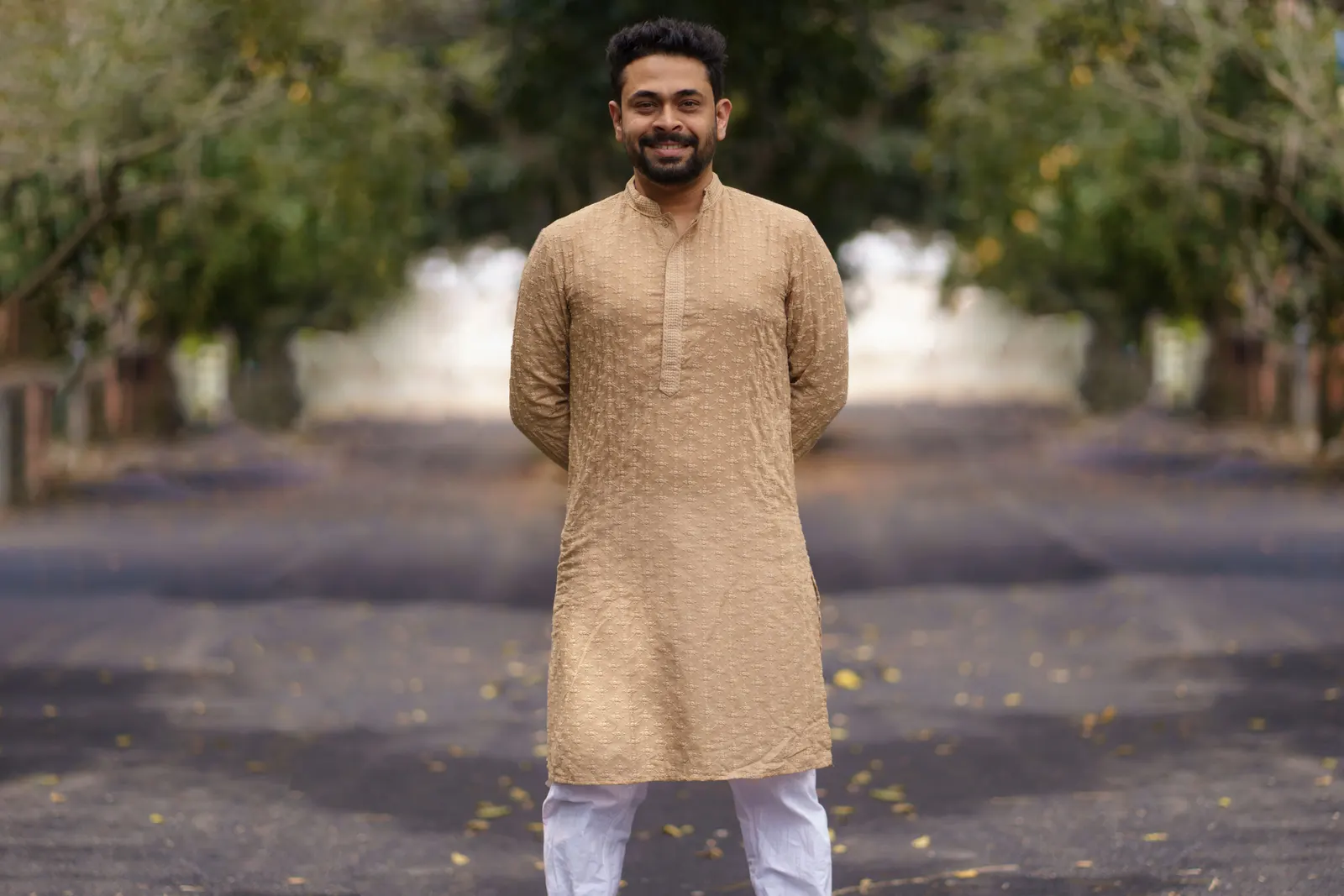 A man in a beige kurta standing on a leafy avenue