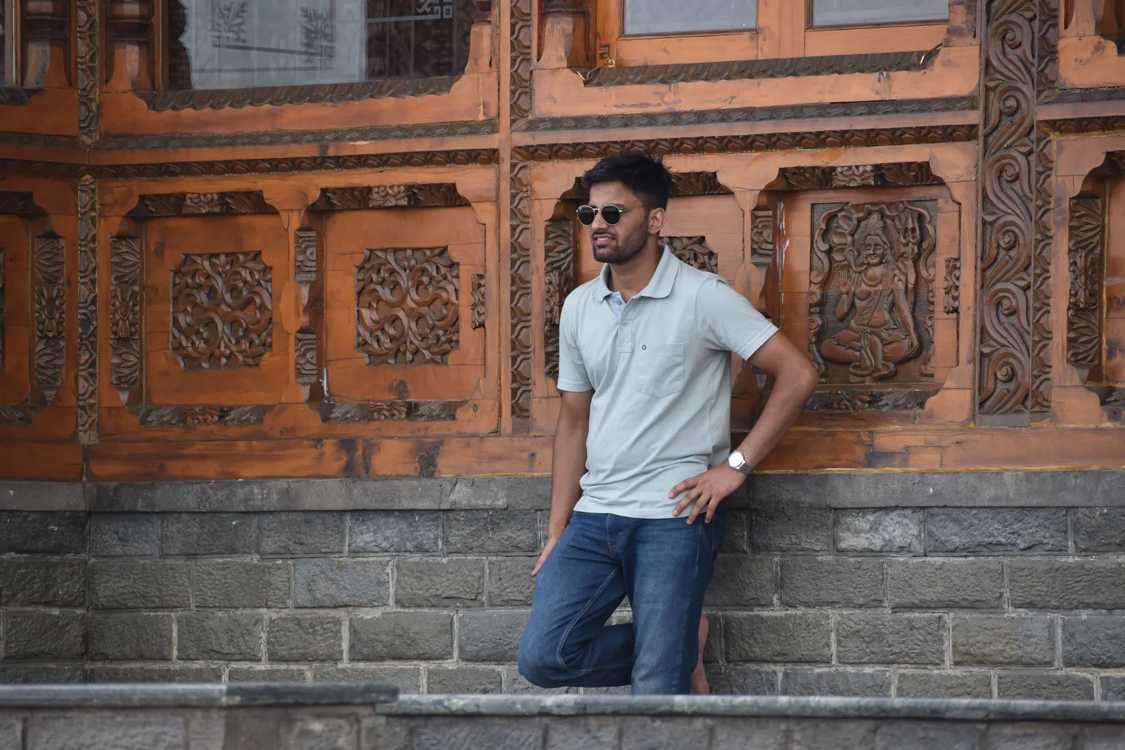 A man in a grey polo and jeans leaning on a carved stone wall