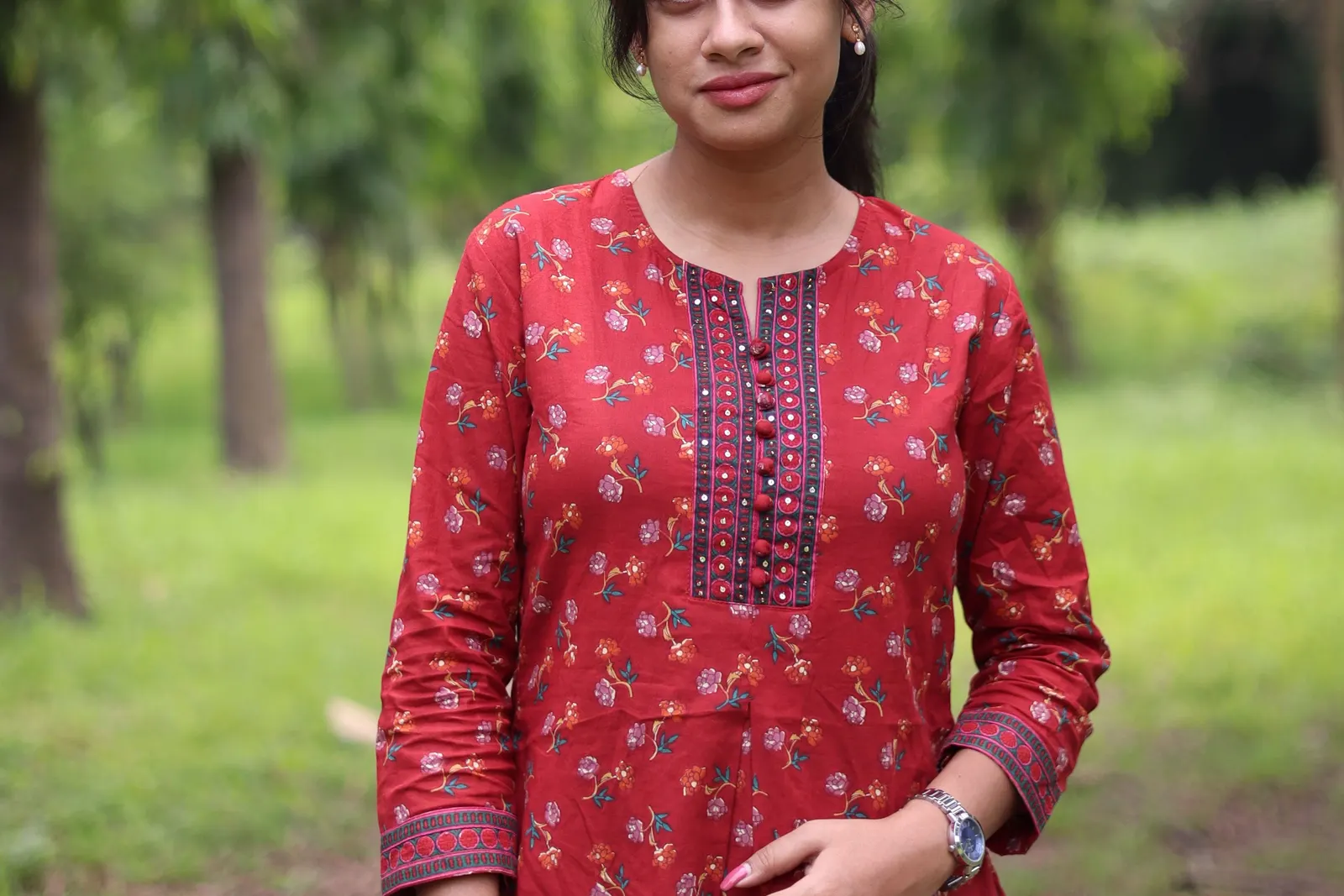 A woman in a red printed kurta standing among trees