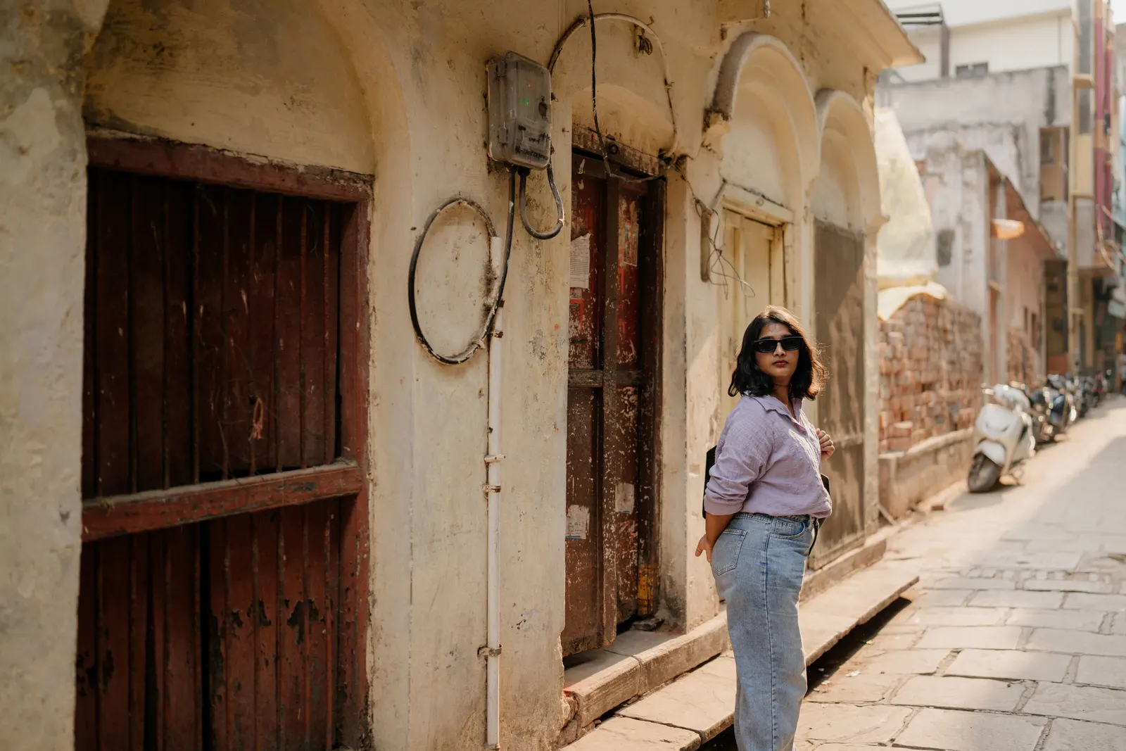 A woman in a lilac shirt and jeans standing in an old lane